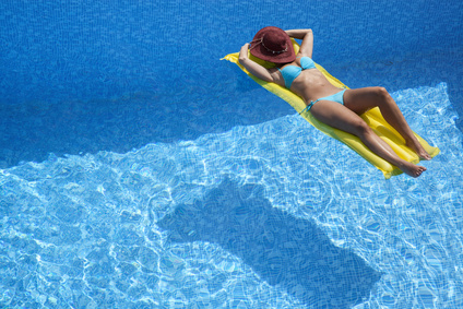 Frau mit Hut entspannt auf Luftmatratze im Pool