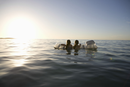 Zwei Mädchen mit Luftmatratze schwimmen in Richtung Horizont