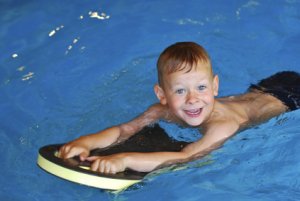 Junge schwimmt in Schwimmbad mit Schwimmbrett und hat Spaß
