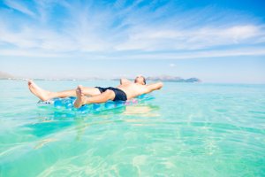 Junger Mann entspannt auf blauer Luftmatratze bei schönem Wetter auf dem Wasser