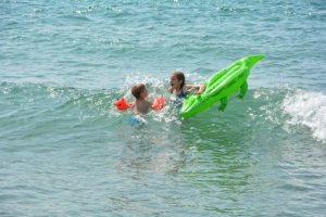 Zwei Kinder spielen mit grüner Korokodil Luftmatratze im Meer