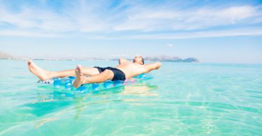 Junger Mann entspannt auf blauer Luftmatratze bei schönem Wetter auf dem Wasser